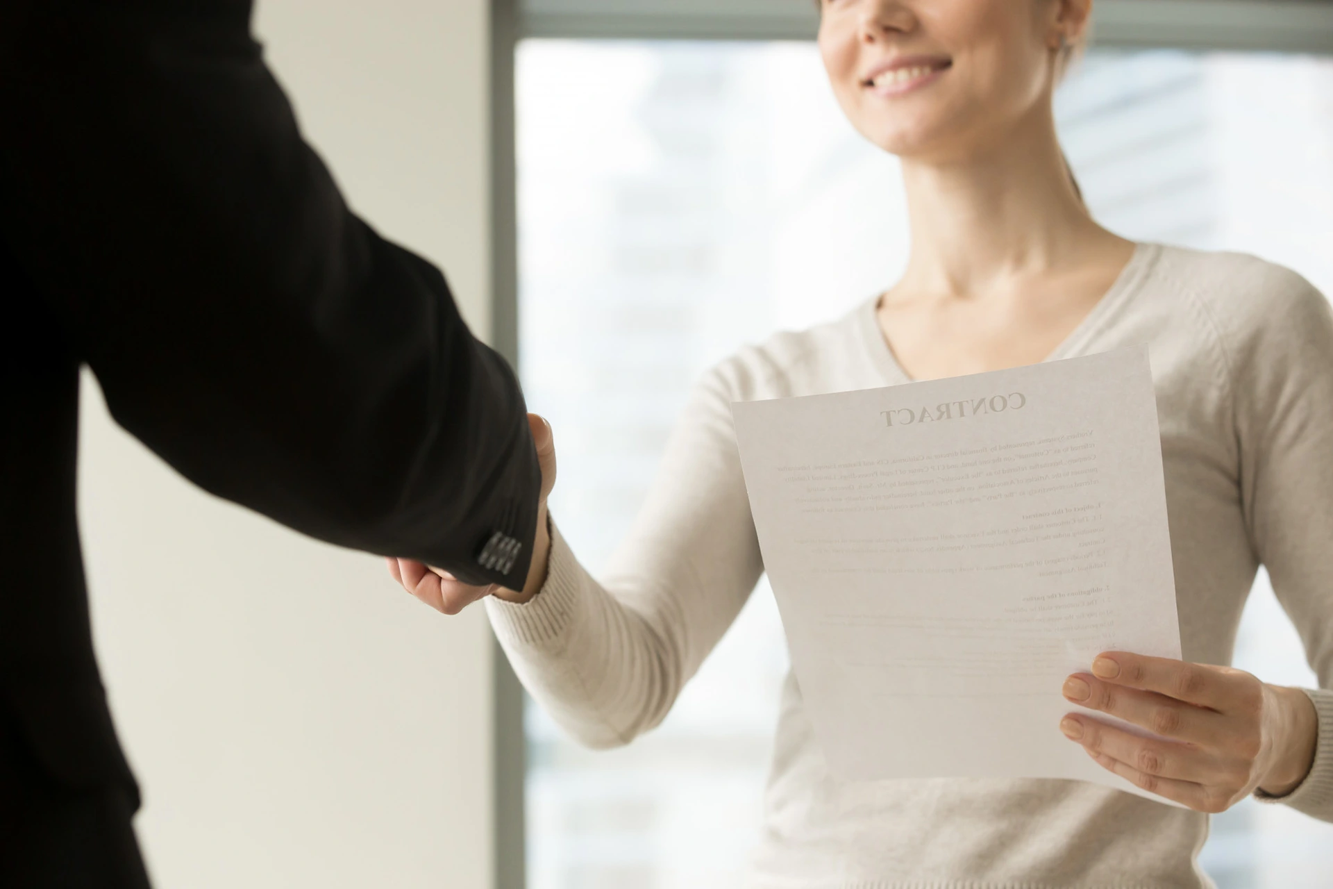 Une femme qui tient son contrat de travail dans la main et serre la main de son RH à Paris