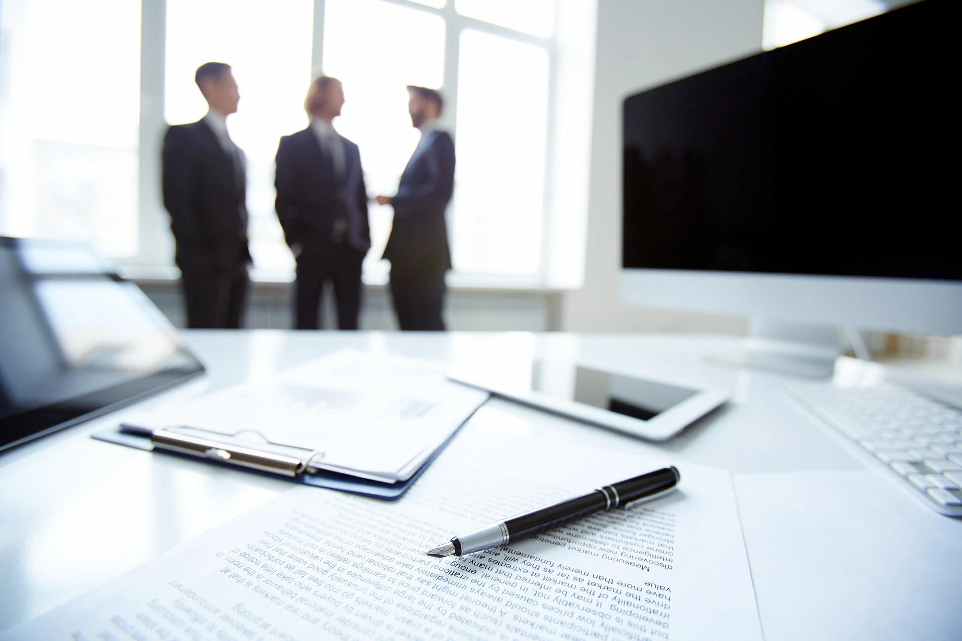 Des hommes d'affaires en arrière-plan qui discutent et au premier plan un bureau avec des contrats